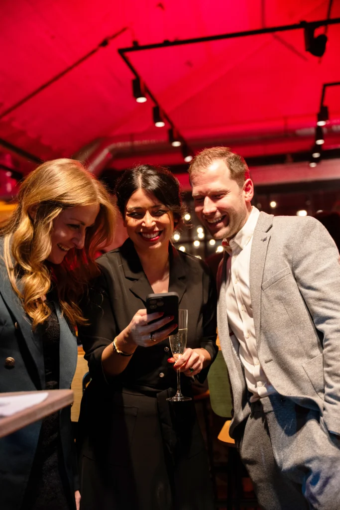 Drei Personen schauen lächelnd auf das Handy der mittleren Person